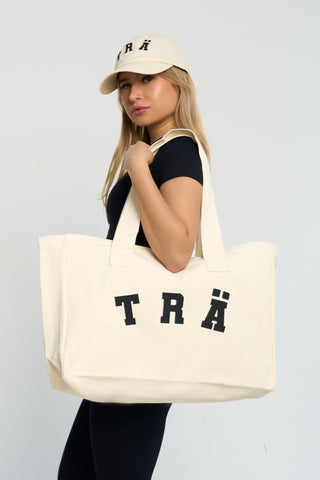 TRÄ canvas tote with black logo, zip closure, and inside pocket.